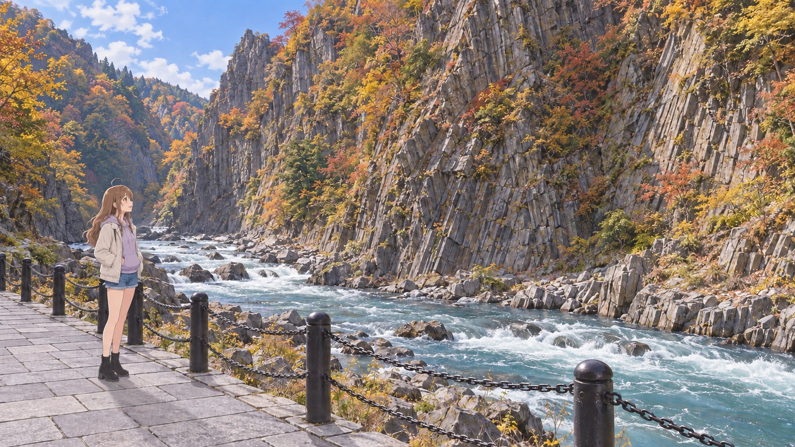 At Kiyotsu Gorge in autumn, a woman in a lavender hoodie with a jacket layered over it stands behind a black chain barrier with both hands in her pockets, looking across the Kiyotsu River at a wall of columnar rock.