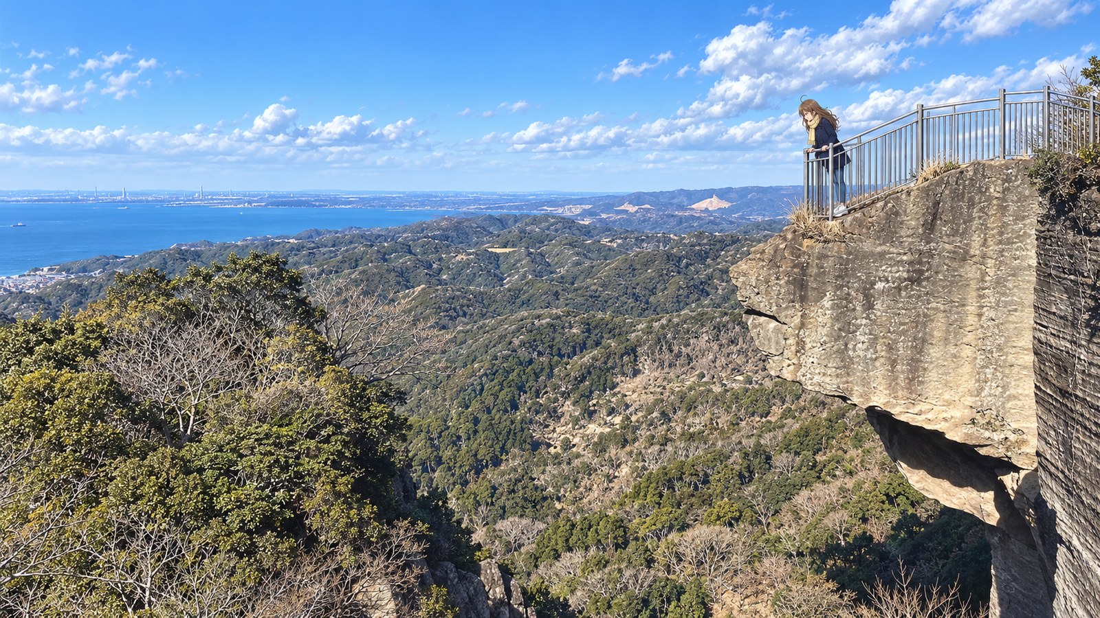 谷へ突き出した鋸山の地獄のぞきの岩の先で、柵の手すりを両手で握って下をのぞく主人公。奥に房総の山並みと東京湾